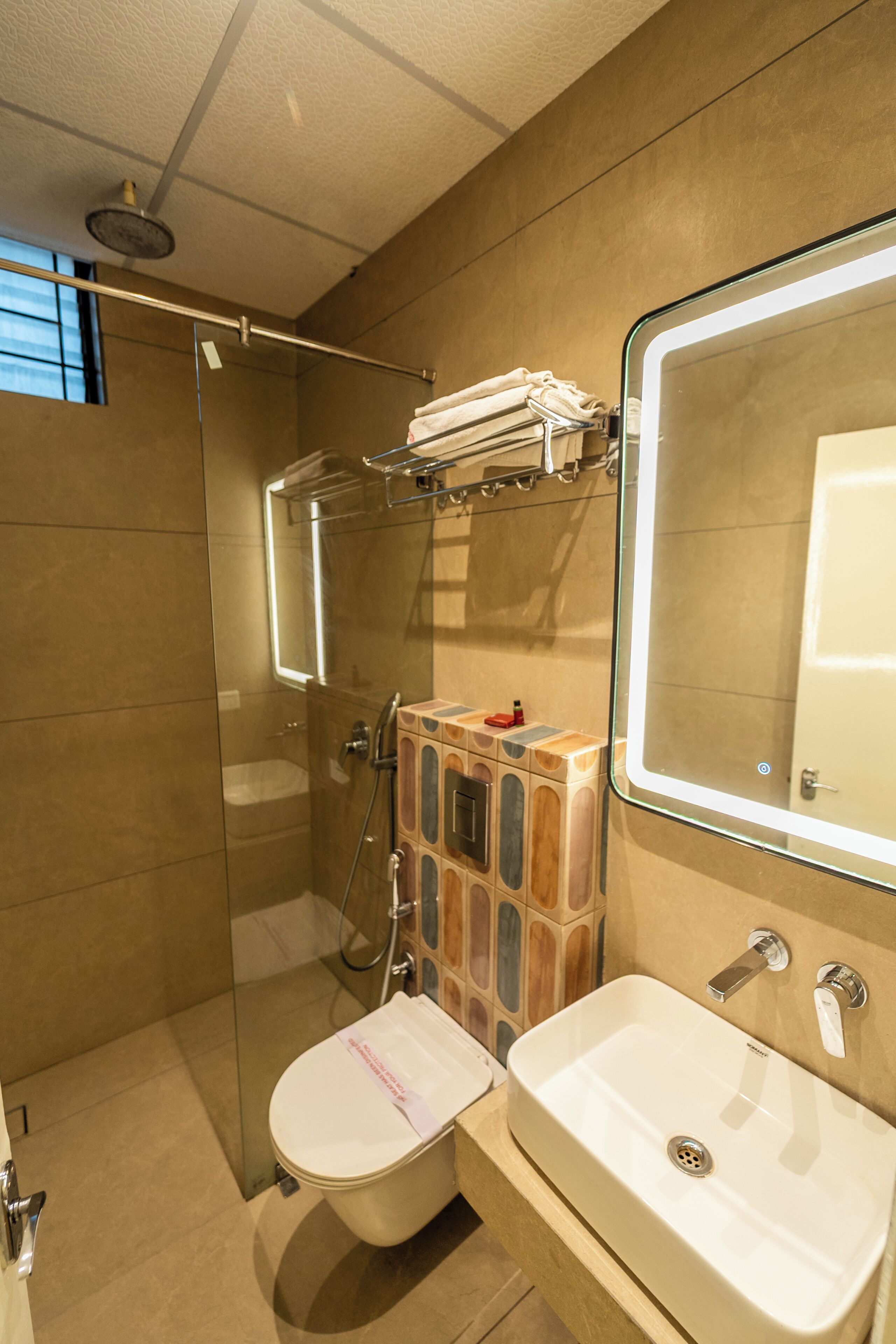 A modern bathroom with a glass shower enclosure, a white sink, and a mirror with integrated lighting.
