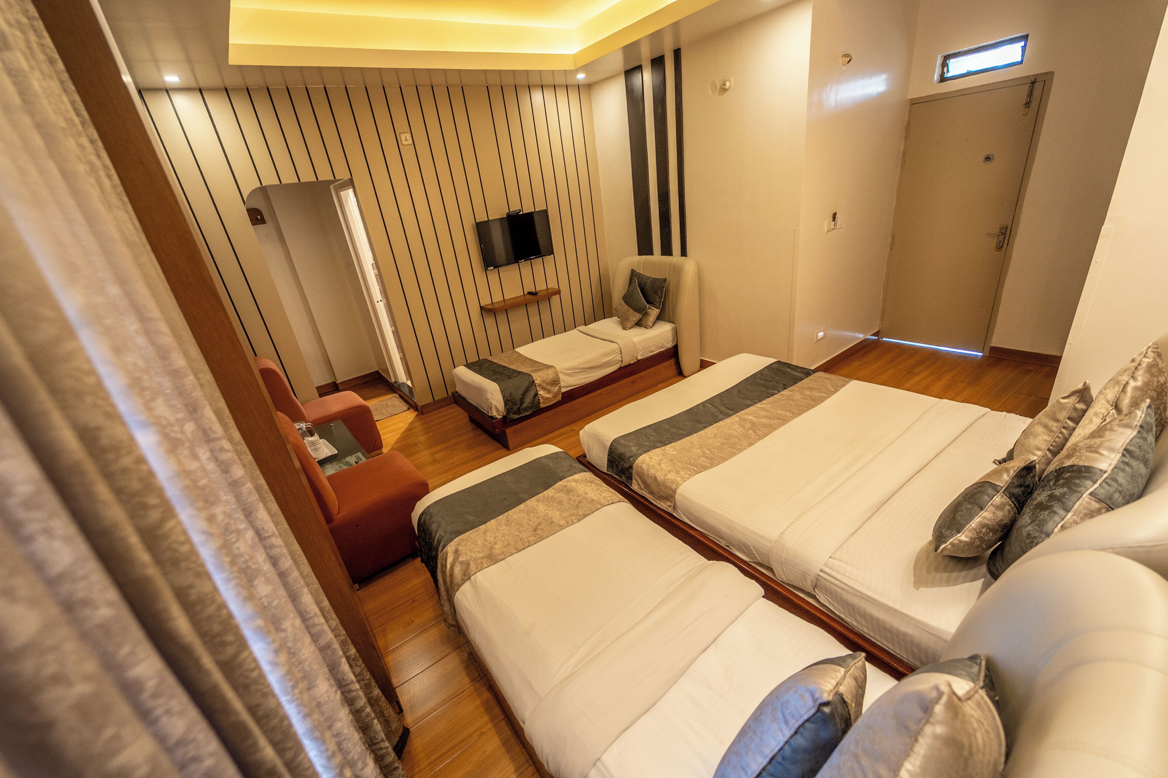 A hotel room with two beds, a TV, a small seating area, and a wardrobe.