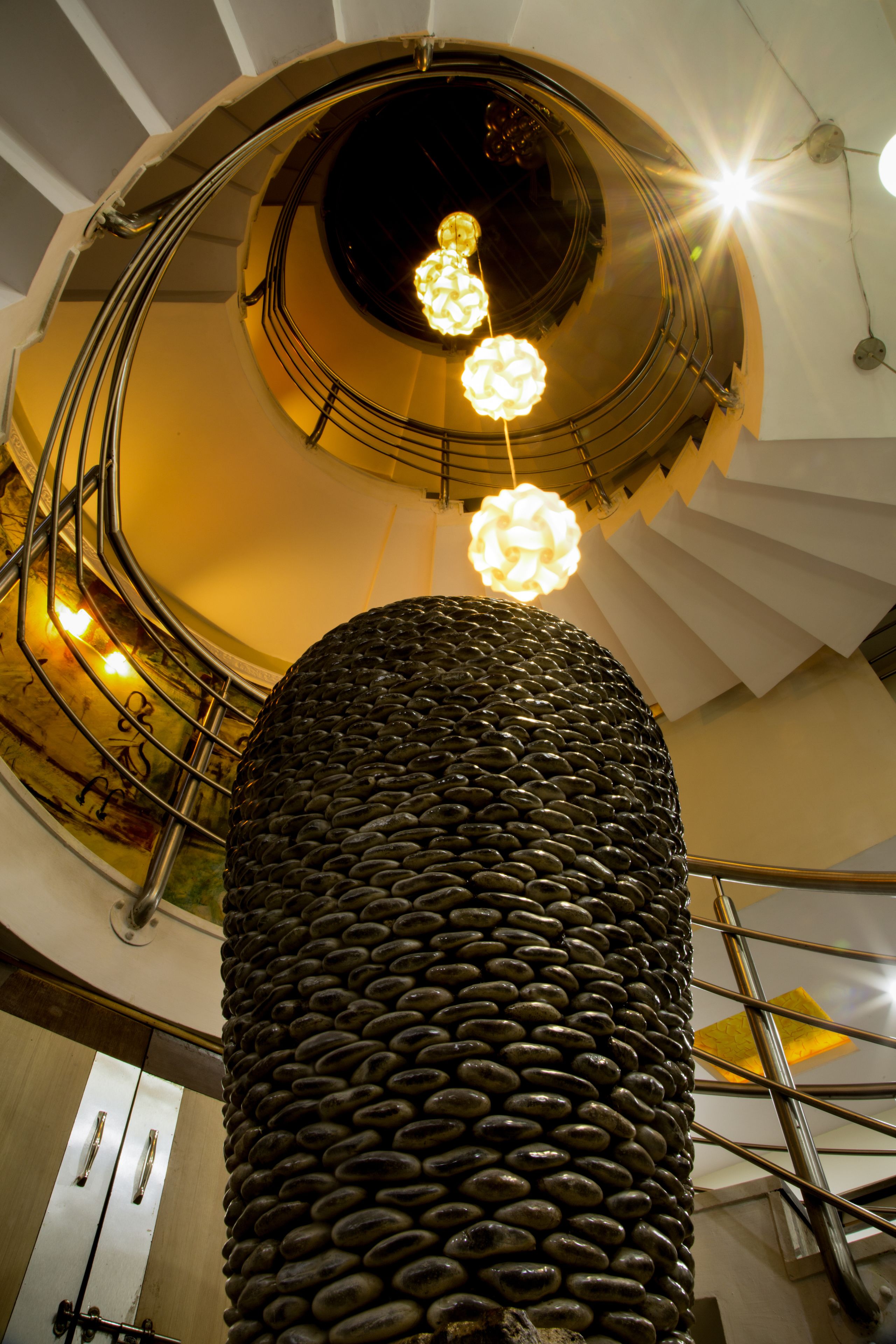 A spiral staircase with a central column of stacked stones and three spherical light fixtures.