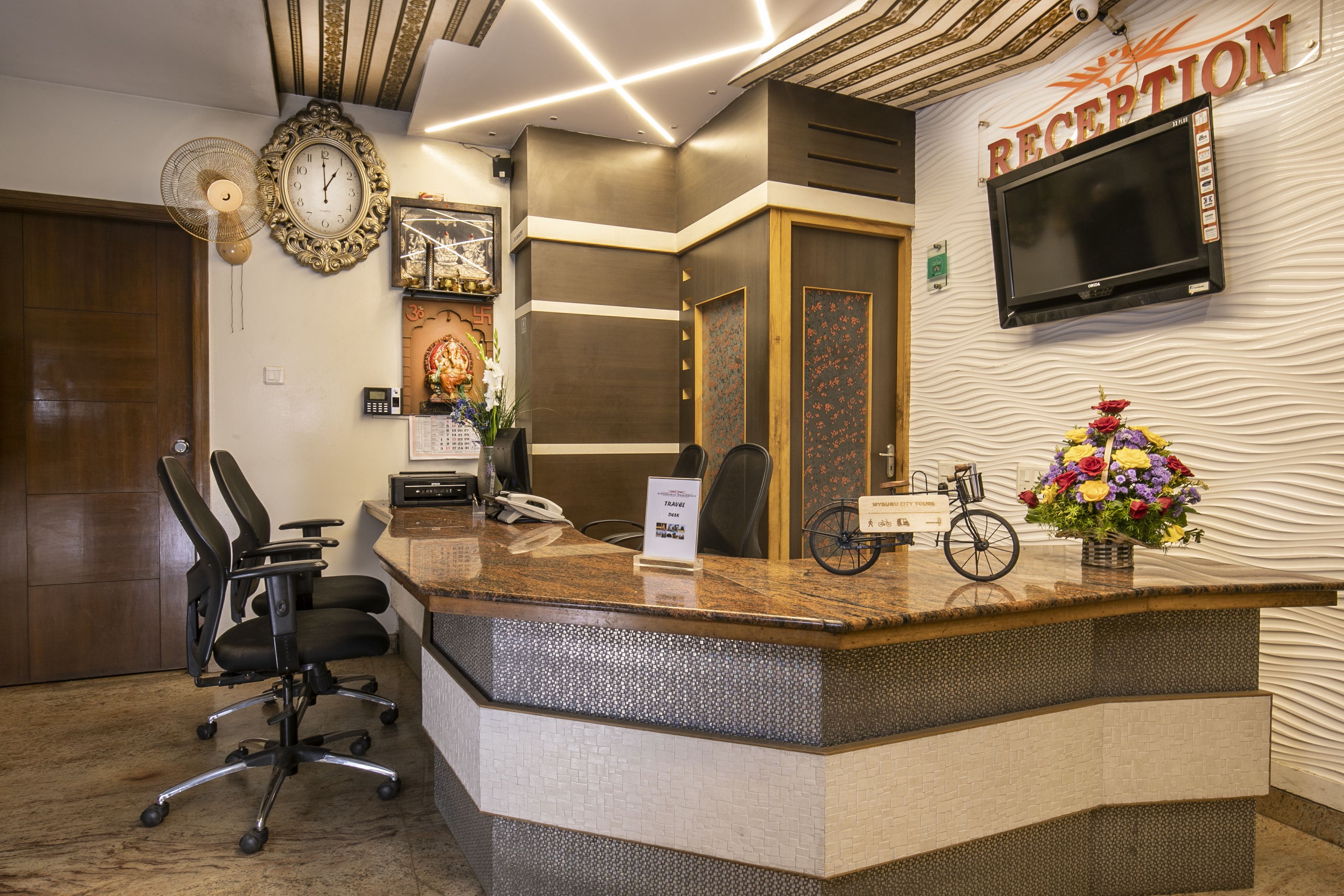 A reception area with a reception desk, a television mounted on the wall, a clock, and a sign indicating the reception.