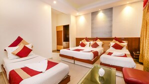A hotel room with four beds arranged in a U-shape, a glass coffee table, and a red chair. - Aishwarya Residency (Mysore)