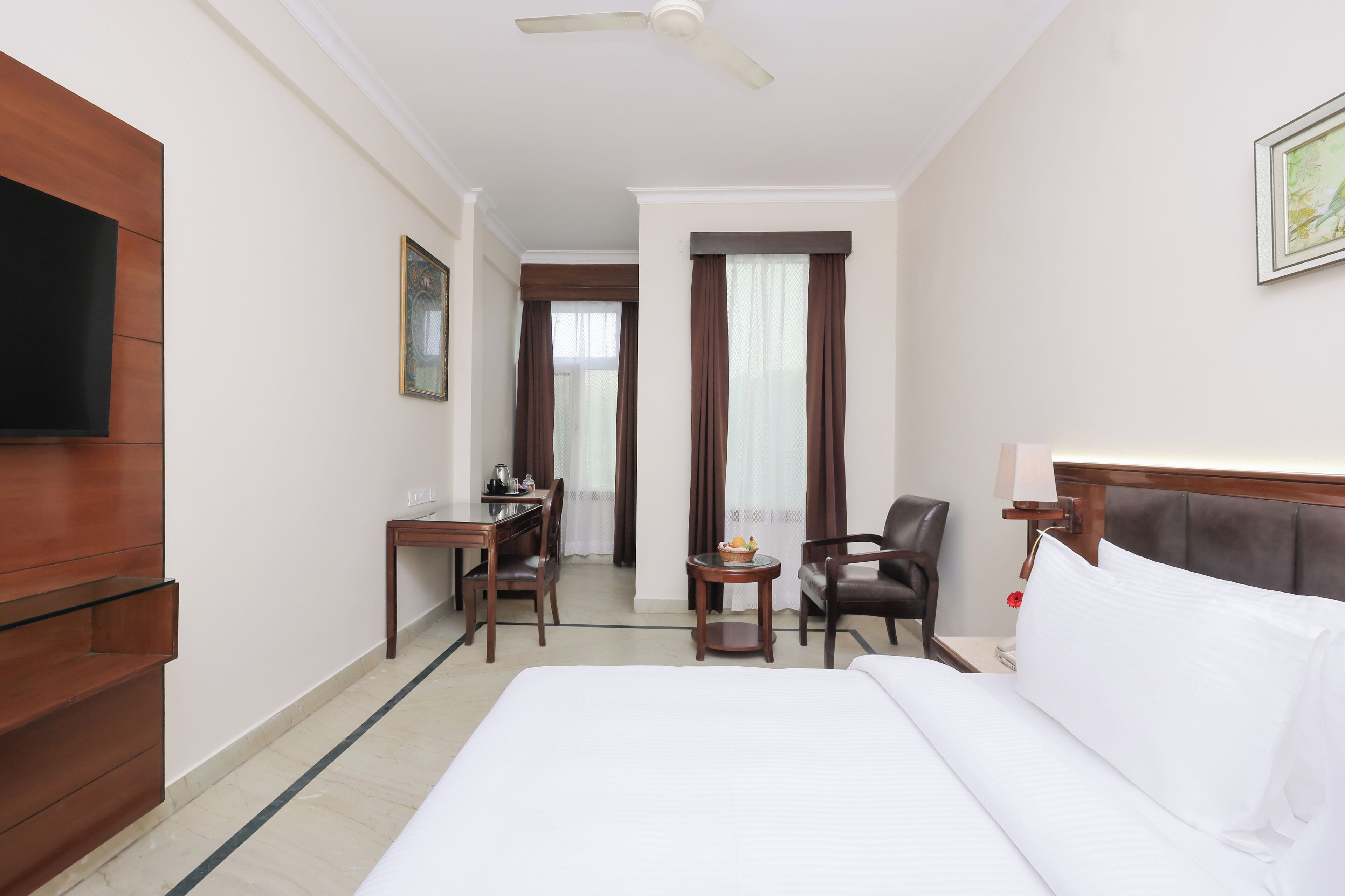 A hotel room with a bed, a desk, a chair, a TV, and a window with curtains.