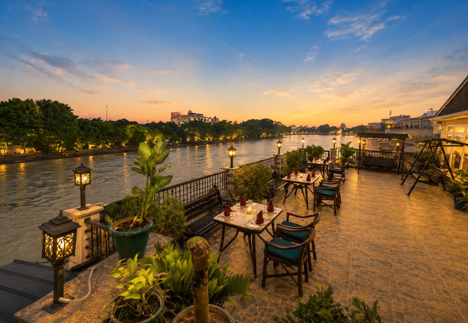 An outdoor dining area with tables and chairs, a river view, and a cityscape in the background.