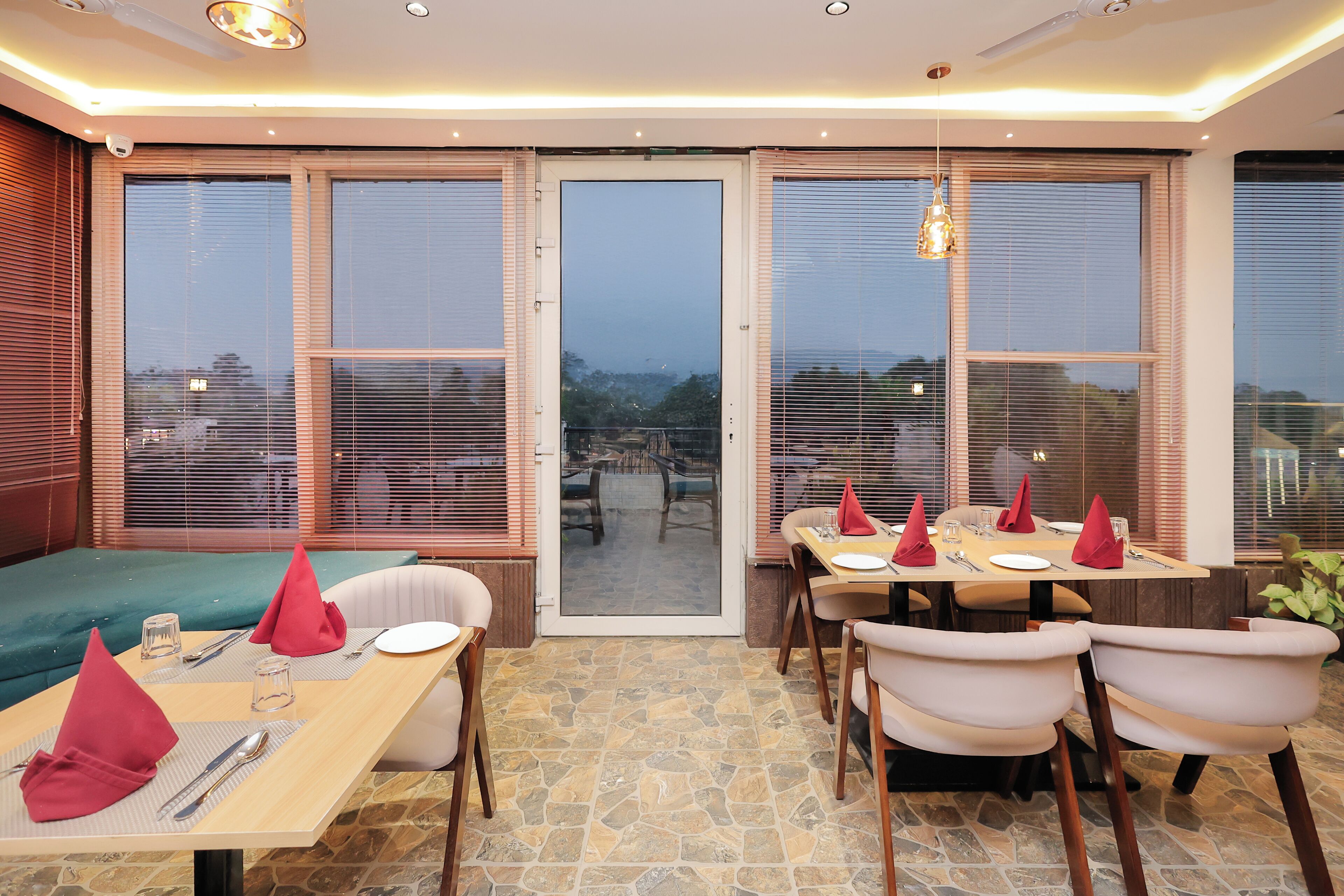Comedor con vistas a la ciudad a través de amplios ventanales, suelo de baldosas de piedra y una lámpara de araña moderna.
