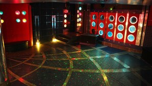 Una habitación con un diseño geométrico en el suelo, una pared roja con lámparas circulares y un techo oscuro.