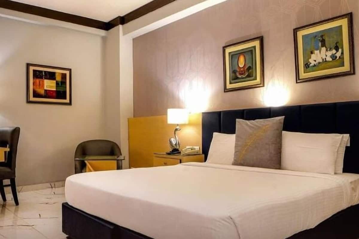 Una habitación de hotel con una cama grande, un escritorio con lámpara y dos cuadros en la pared.
