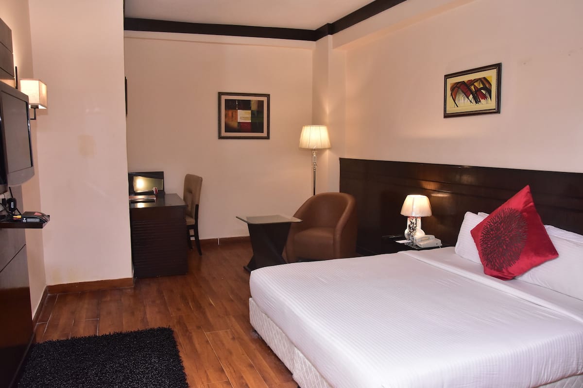 Una habitación de hotel con una cama grande, un escritorio, una silla, un televisor y una lámpara.