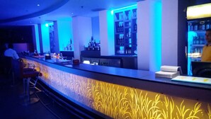 Una zona de bar con mostrador, taburetes y estantes llenos de botellas.