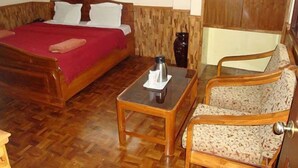 A wooden bed with a red blanket, a small wooden table with a kettle, and a patterned armchair. - Hotel Royal Residency (Gangtok)