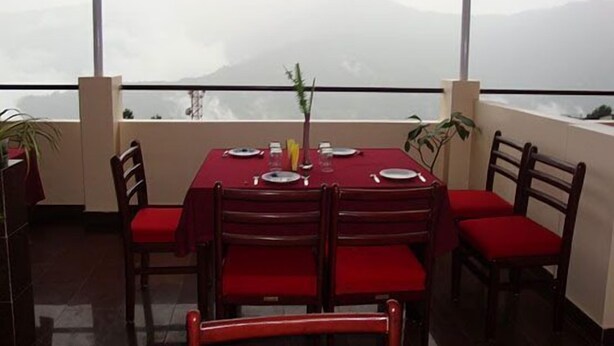 A dining area with a table set for four, chairs, and a view of mountains through large windows. - Hotel Royal Residency (Gangtok)