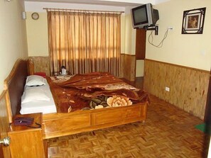 A room with a wooden bed, a television on a stand, a clock on the wall, and a picture frame. - Hotel Royal Residency (Gangtok)