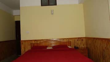 A room with a wooden headboard bed, a red bedspread, and a small window above the bed.