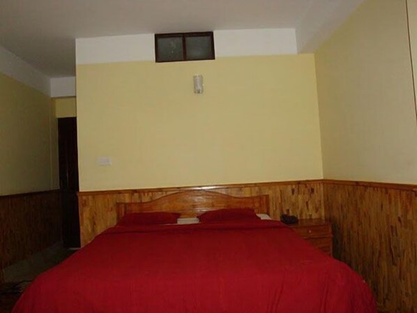 A room with a wooden headboard bed, a red bedspread, and a small window above the bed. - Hotel Royal Residency (Gangtok)