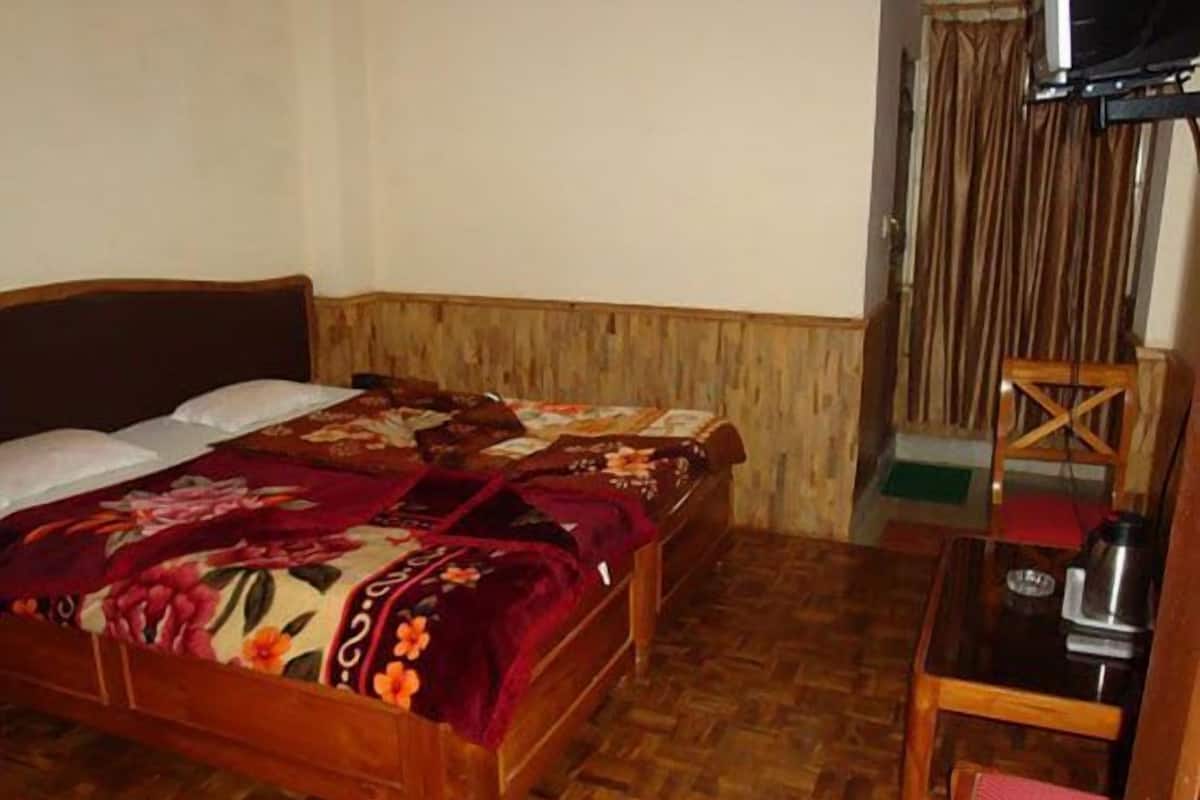 A wooden bed with floral bedding, a wooden nightstand, and a chair with a red cushion.