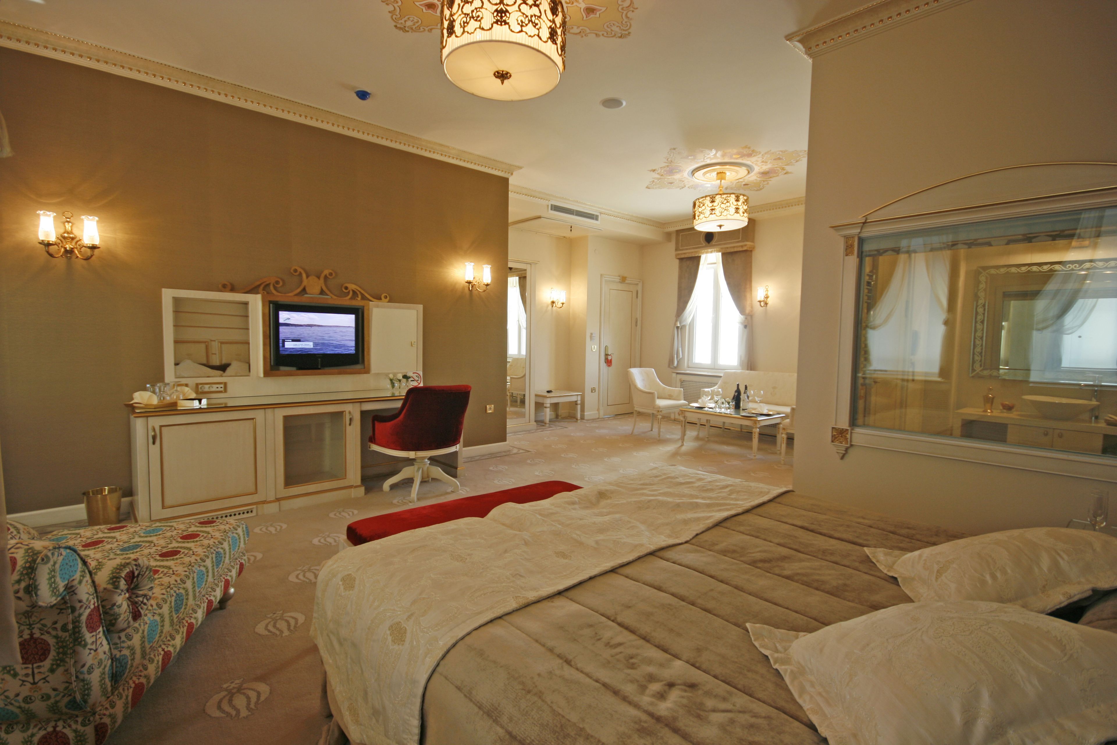 A hotel room with a bed, a desk with a television, a chair, and a window with curtains.