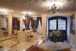 Un lobby lujoso con techo ornamentado, candelabros, un mostrador de recepción y una entrada imponente.