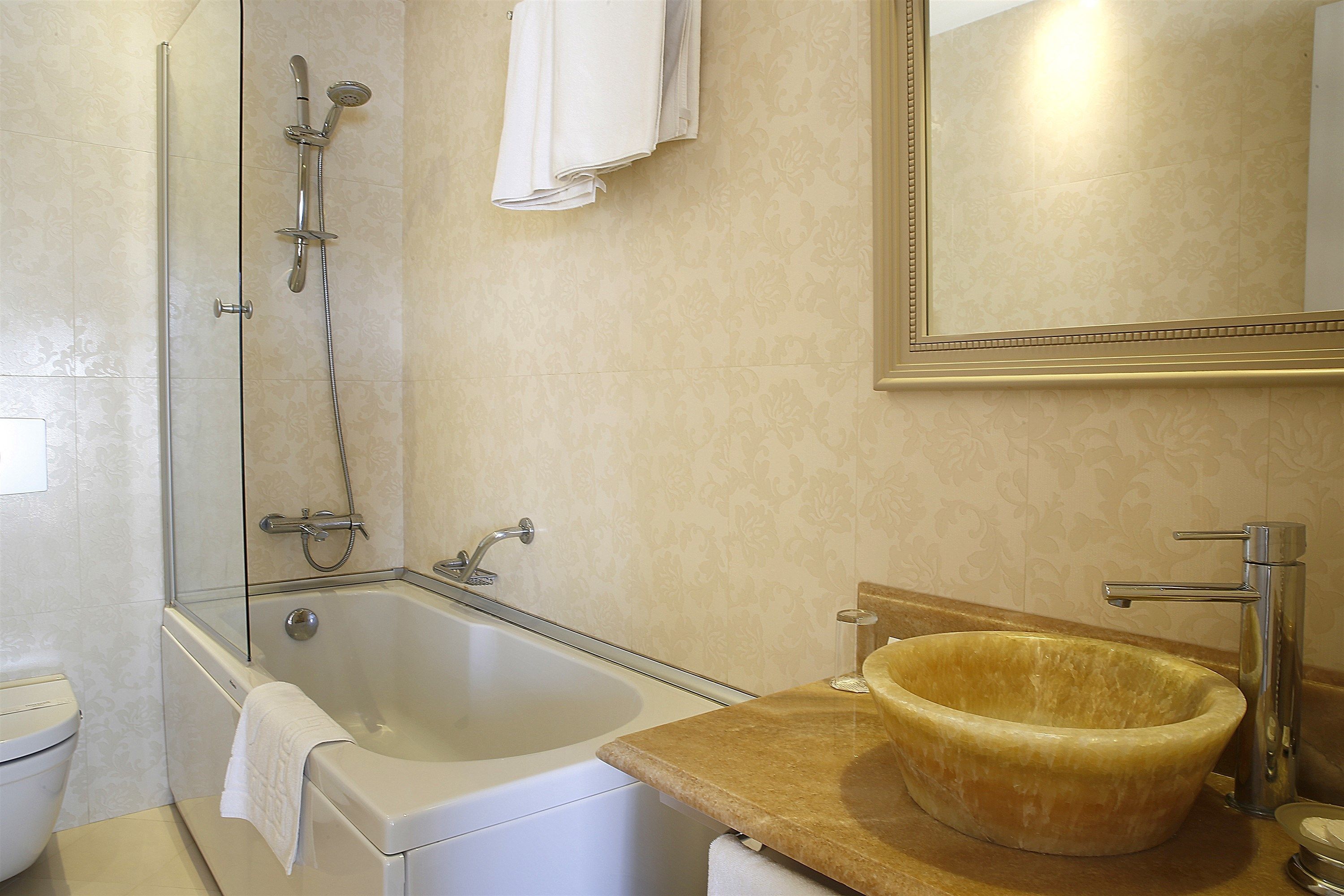 A bathroom with a bathtub, a glass-enclosed shower, a sink with a wooden bowl, and a mirror.