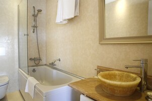 Un baño con bañera, ducha con cerramiento de vidrio, lavabo con un recipiente de madera y espejo.