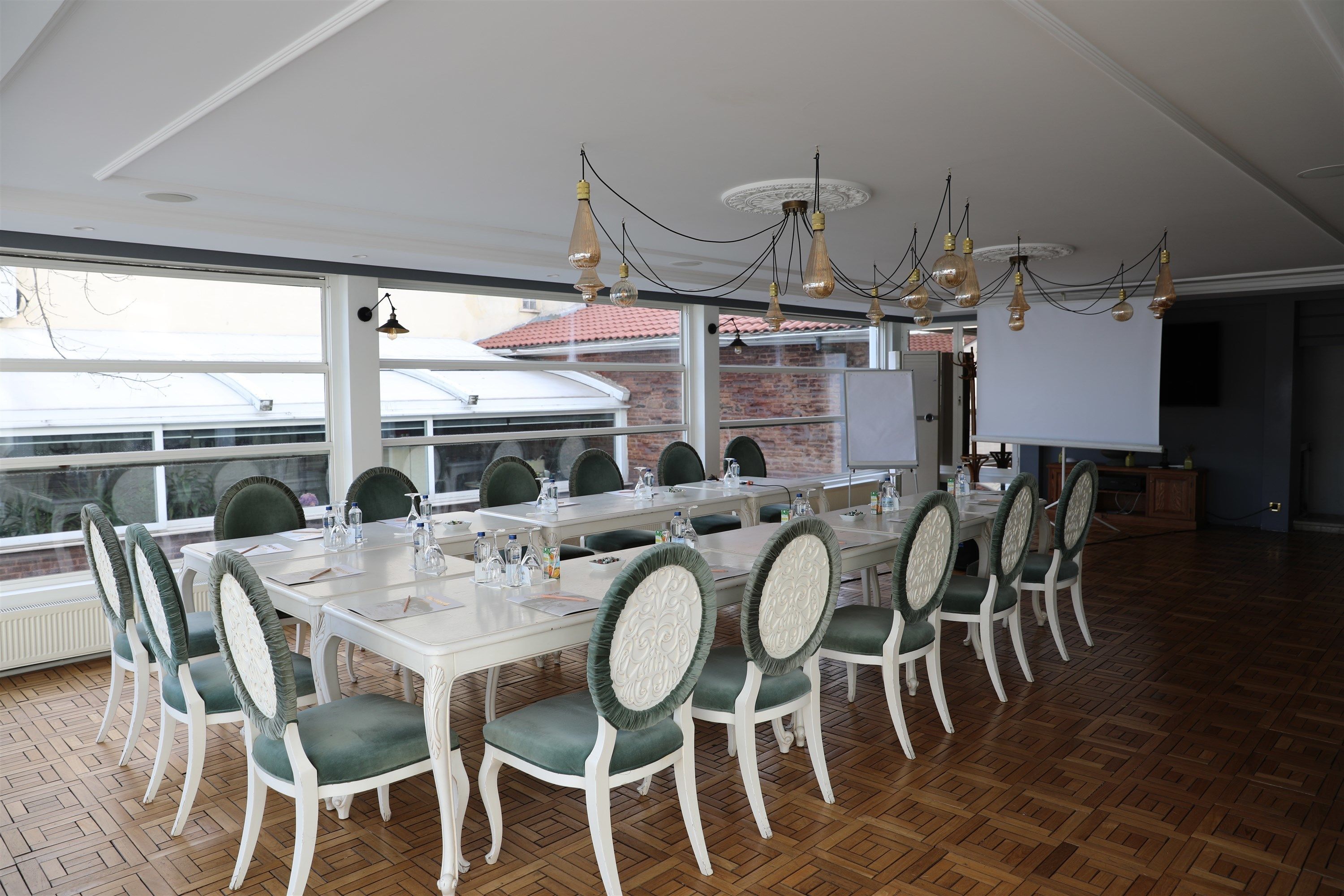 A conference room with a long table, green upholstered chairs, and pendant lighting.