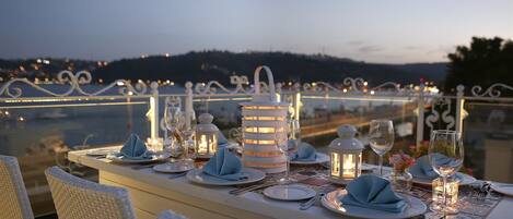 Mesa lista para comer con sillas blancas, mantel blanco y vista de la ciudad al fondo.