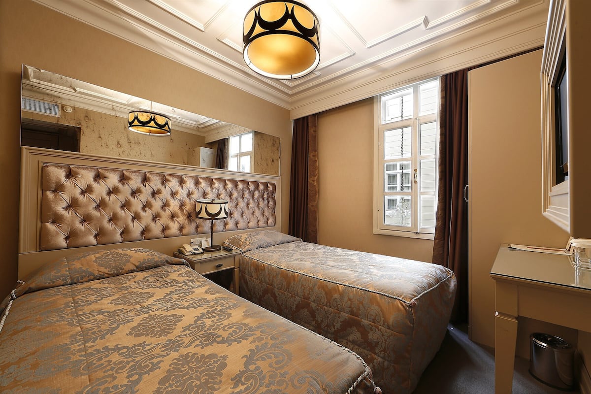 A hotel room with two beds, a large mirror, a desk, and a window with curtains.