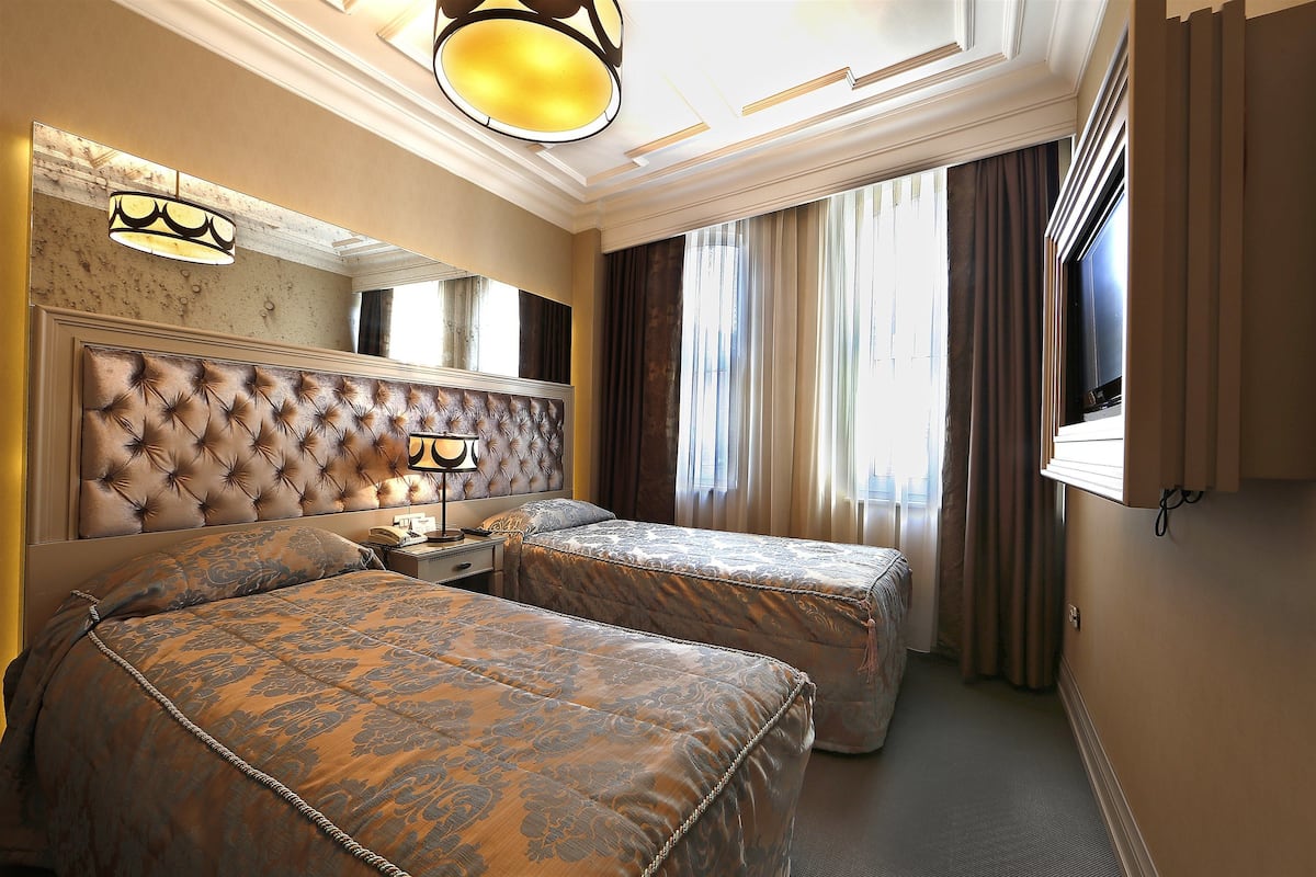 A hotel room with a large bed, a smaller bed, a nightstand, a lamp, a mirror, and a window with curtains.
