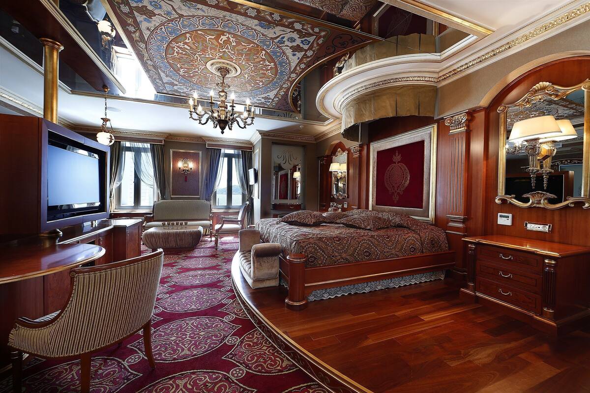 A luxurious bedroom with a large bed, a television, a desk, and a chandelier.