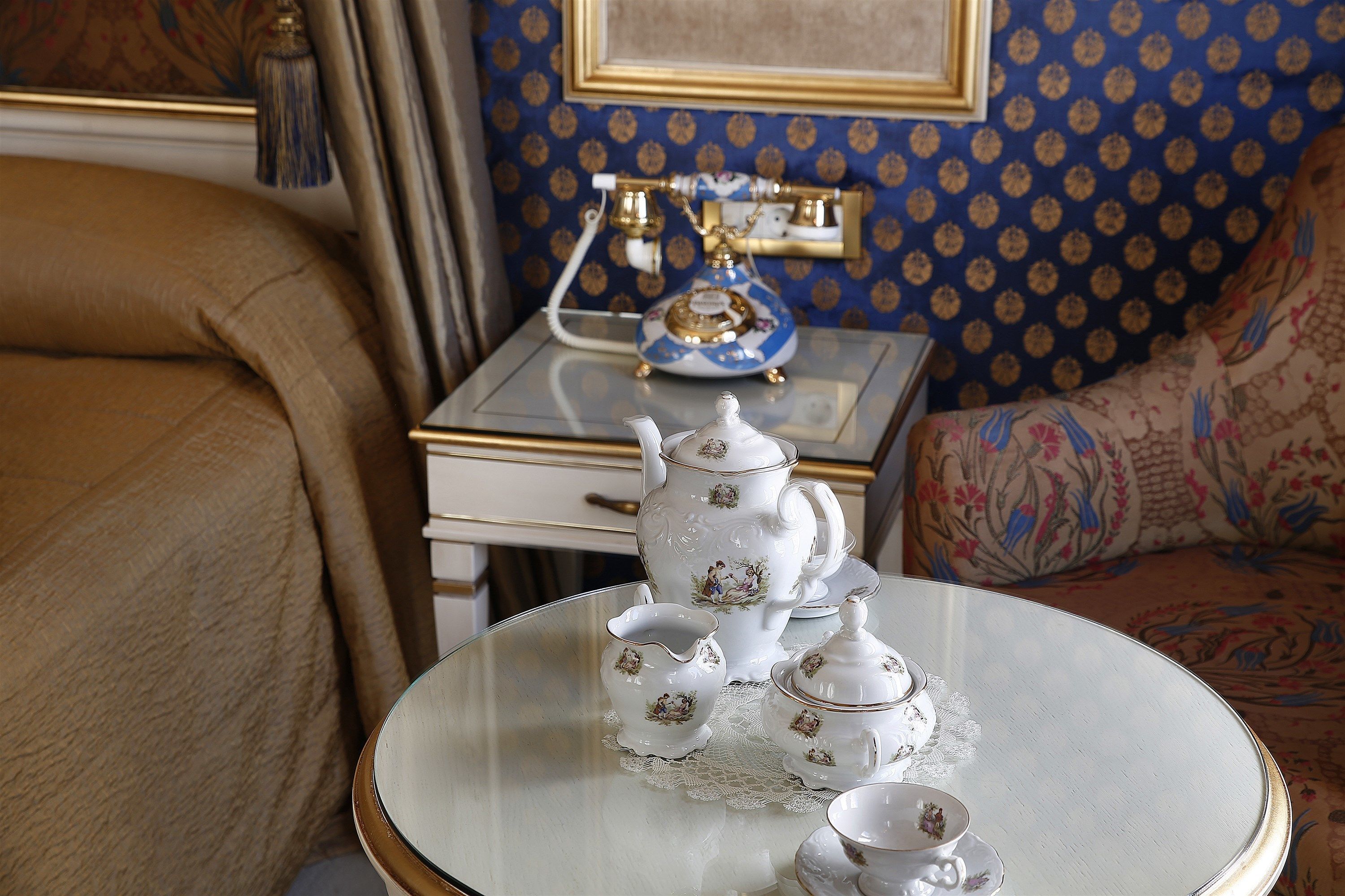 A room with a glass table displaying a tea set, a patterned blue wall, and a patterned sofa.