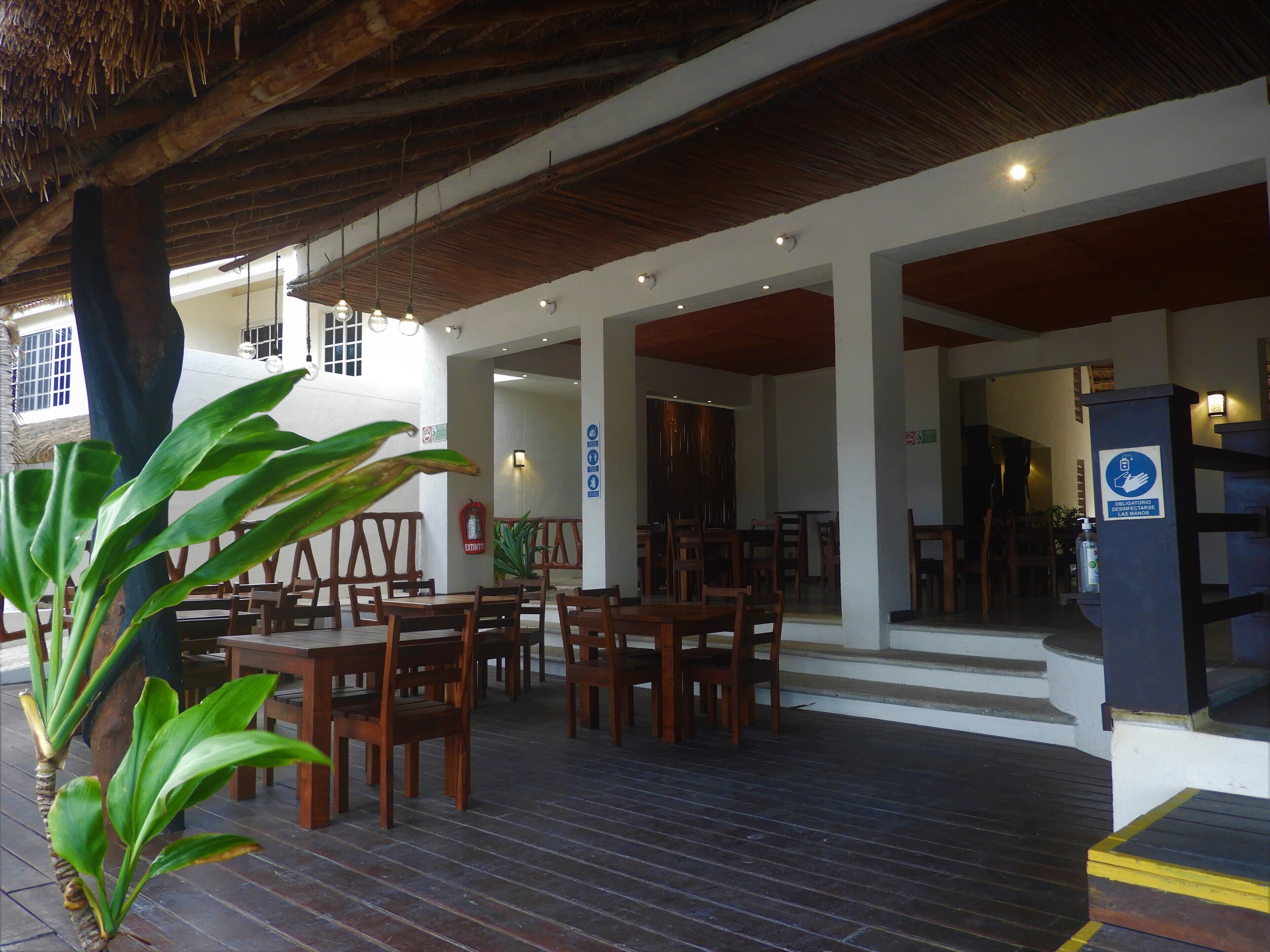 A restaurant with wooden tables and chairs, a thatched roof, and a sign indicating hand sanitizer availability.