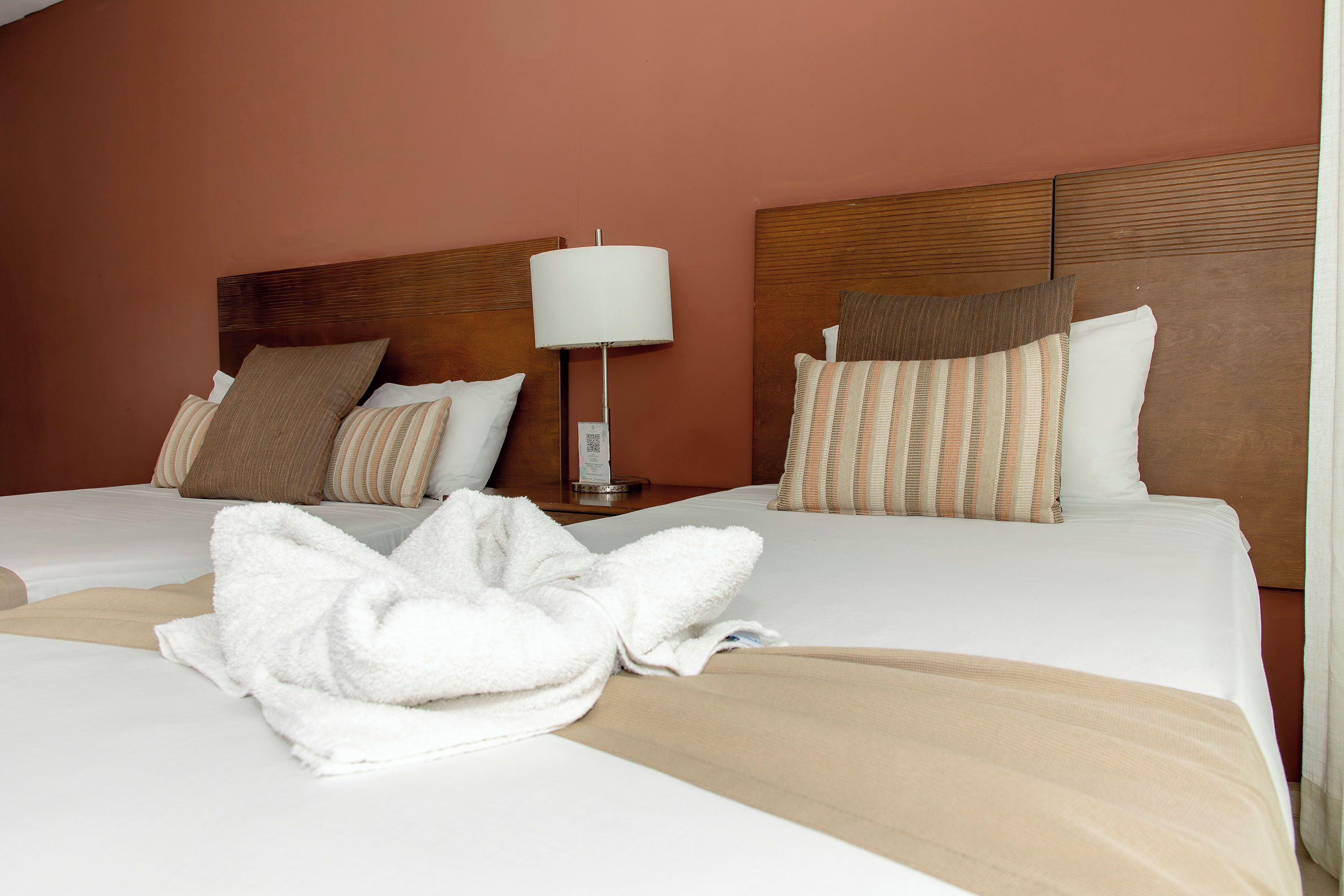 A hotel room with two beds, a nightstand with a lamp, and a robe on the bed.