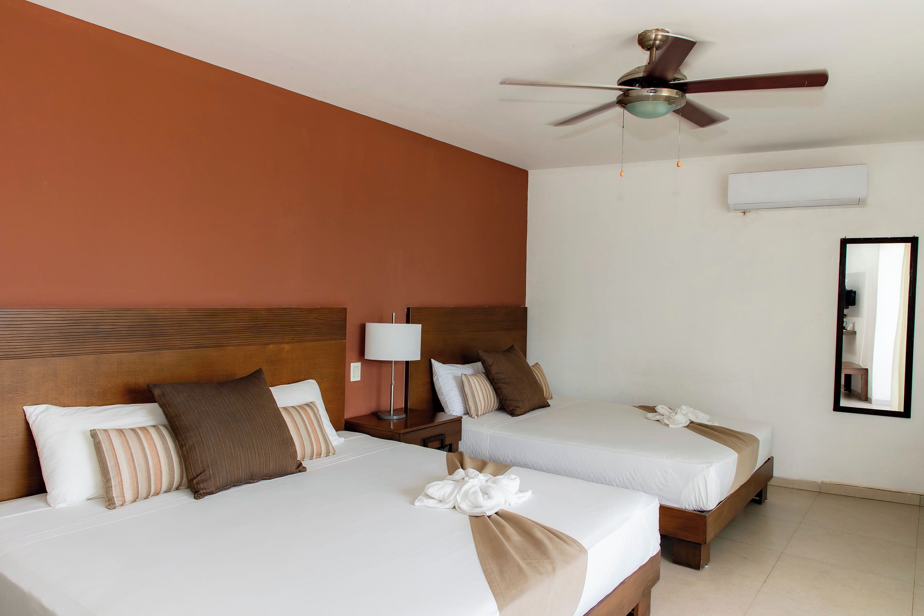 A hotel room with two beds, a ceiling fan, an air conditioning unit, and a mirror on the wall.