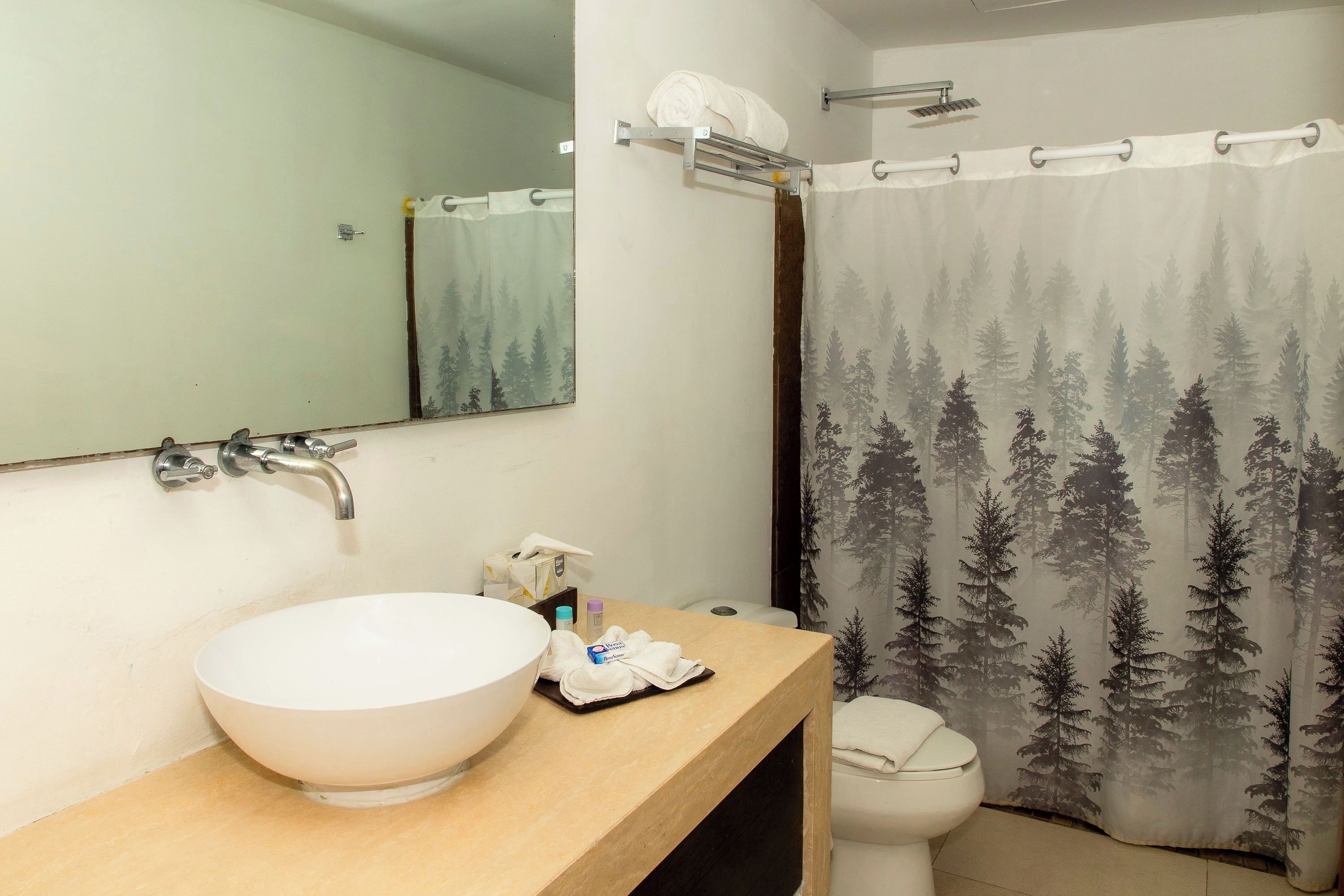 A bathroom with a large white sink, a mirror, a towel rack, and a shower curtain with a forest pattern.