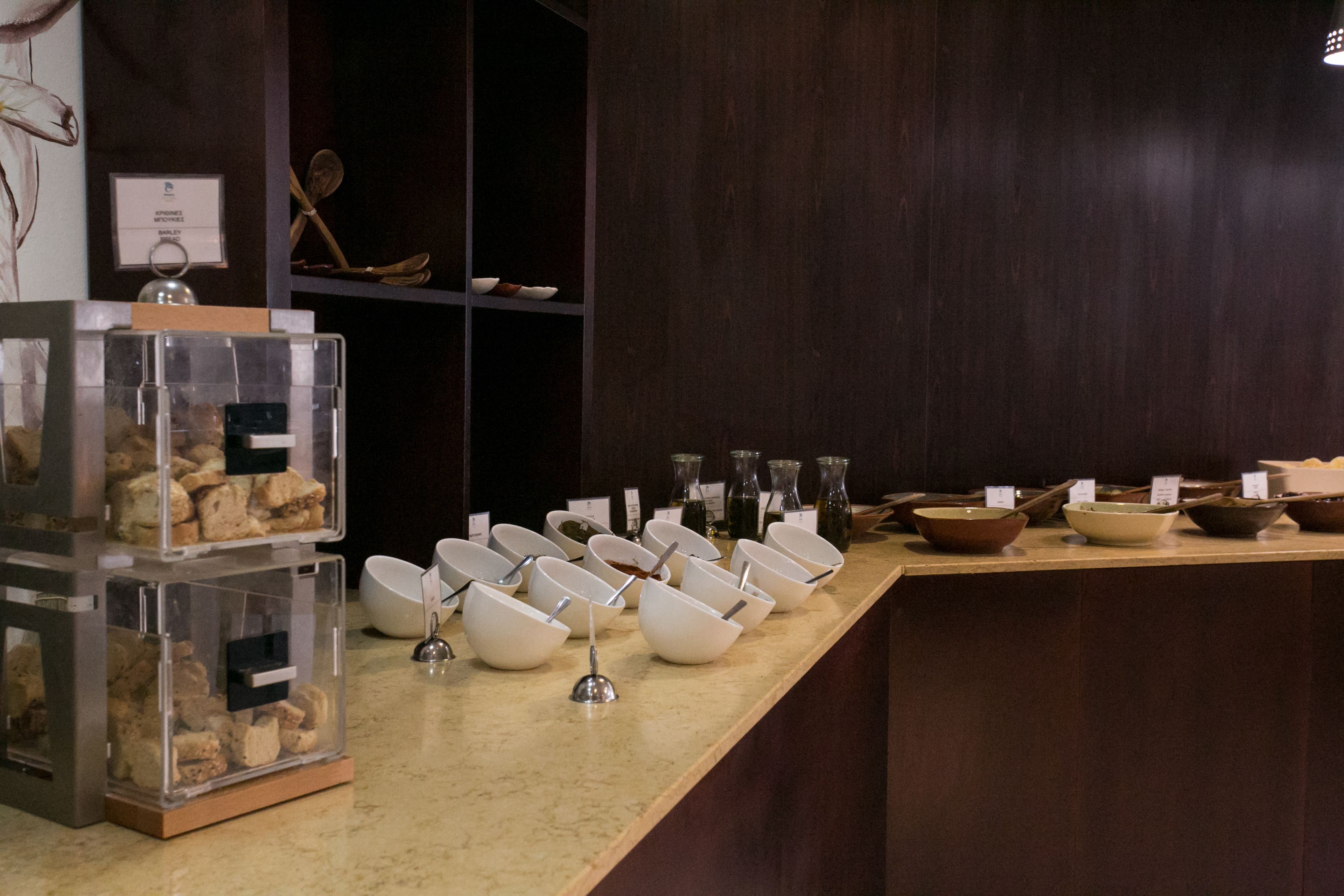 A buffet setup with clear glass containers of food and multiple white bowls with spoons.