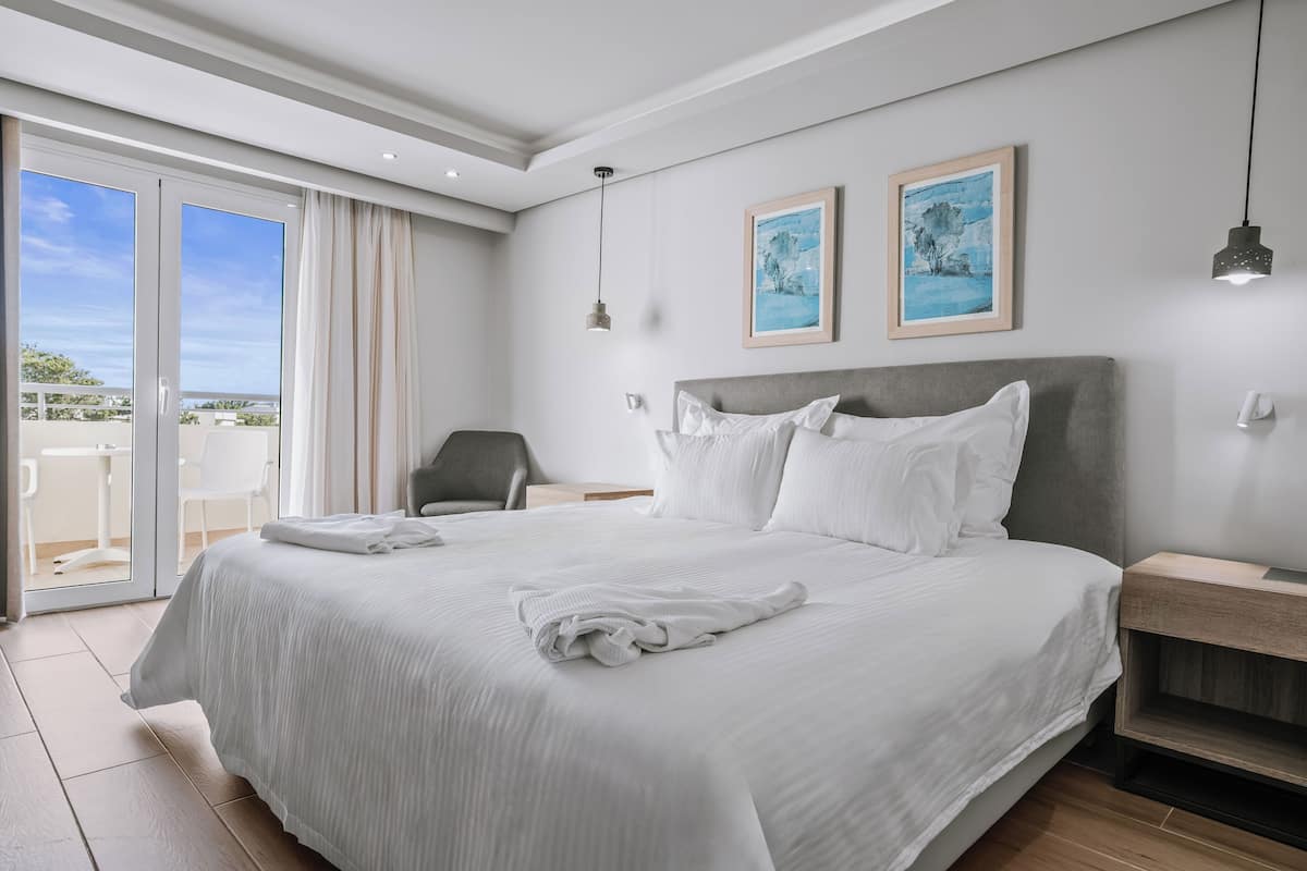 Ein modernes Hotelzimmer mit einem großen Bett, einem Sessel und einem Balkon mit Blick.