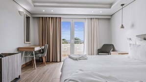 A modern hotel room with a large bed, a desk, a chair, and a balcony with a view. - Almyra Resort (Ierapetra)