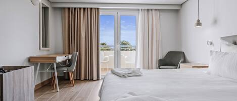 A modern hotel room with a large bed, a desk, a chair, and a balcony with a view.