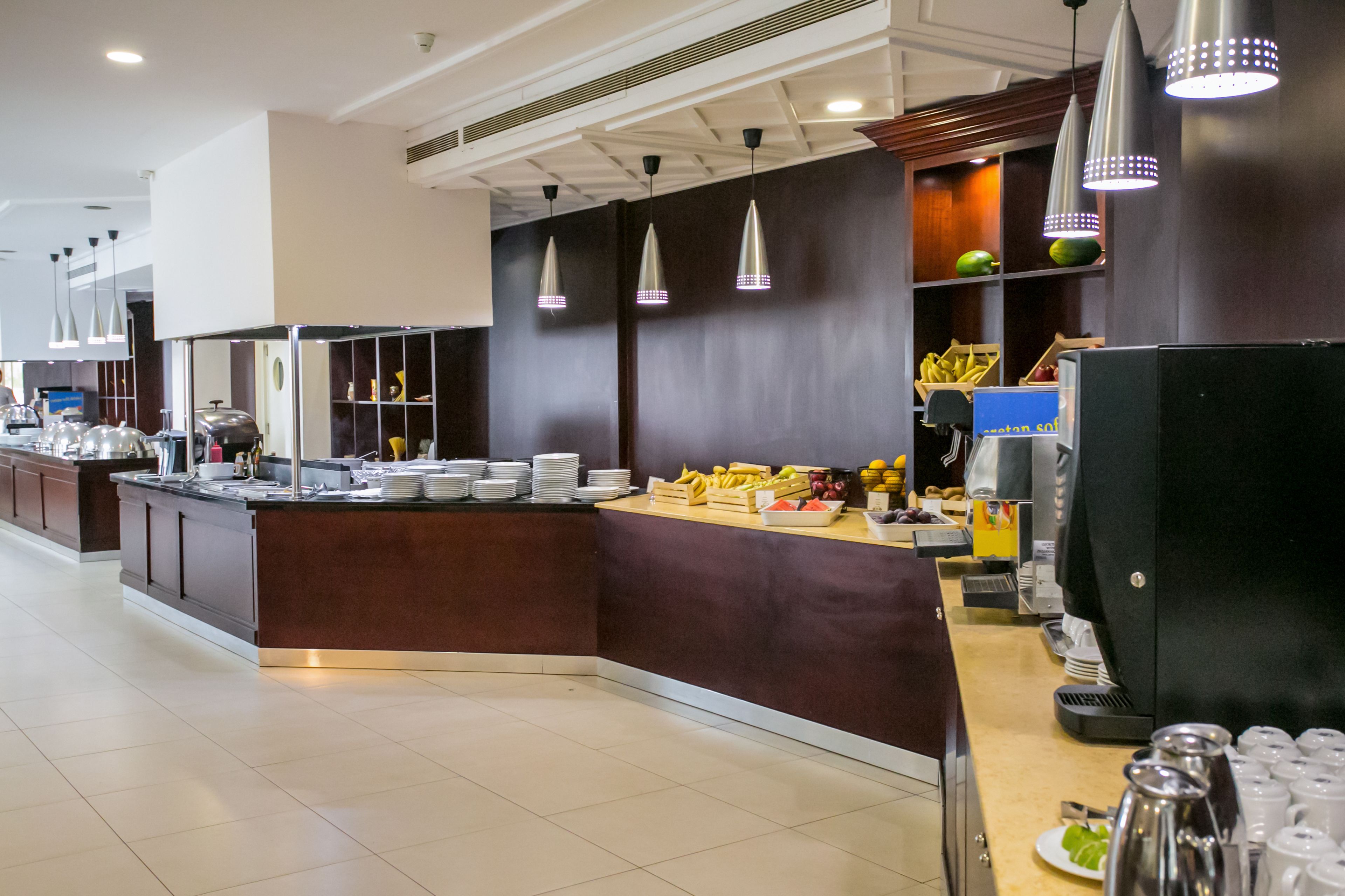 A modern hotel kitchen with a buffet setup, including a variety of fruits and beverages.