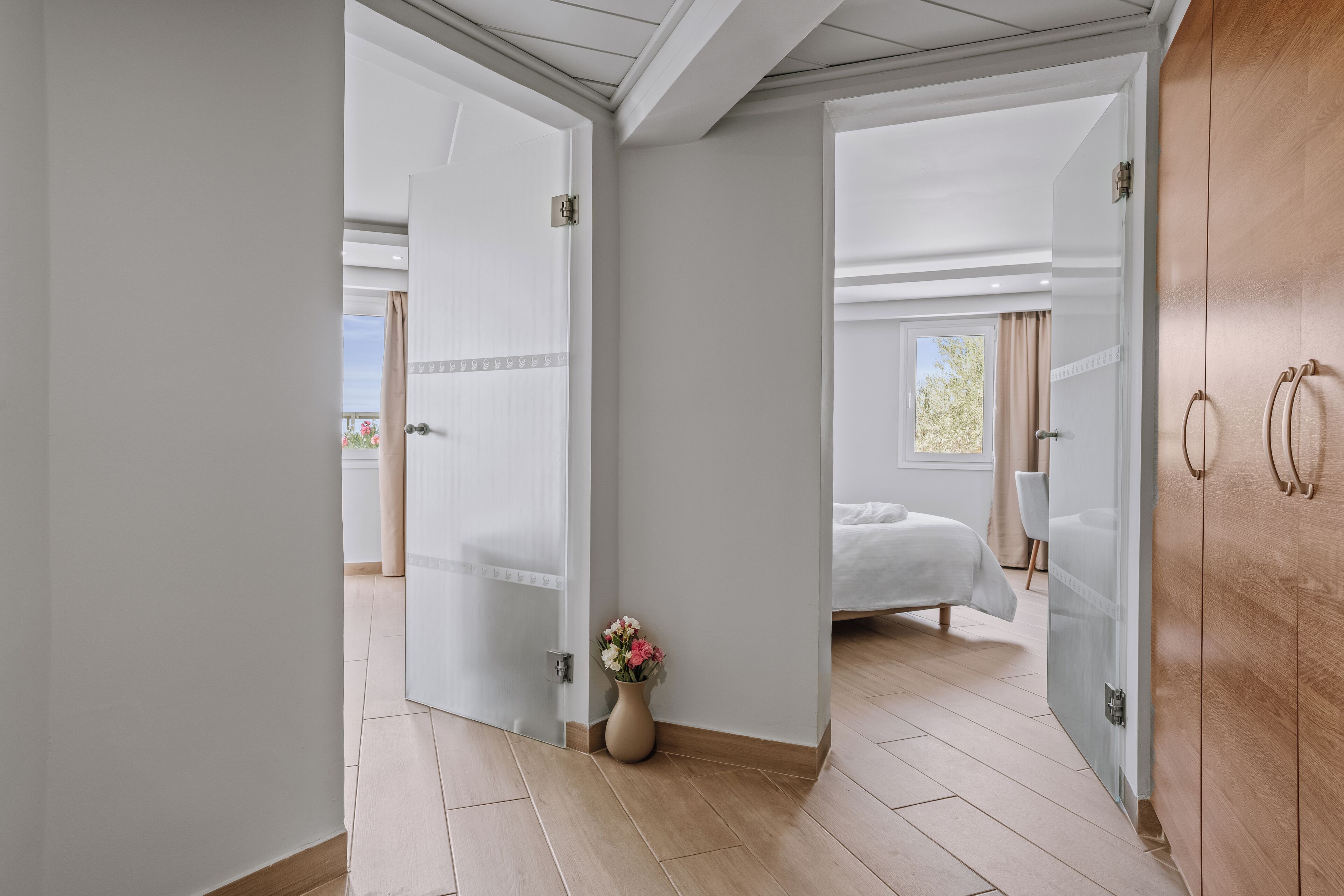 A hotel room with a bed, a wooden wardrobe, and a vase of flowers.