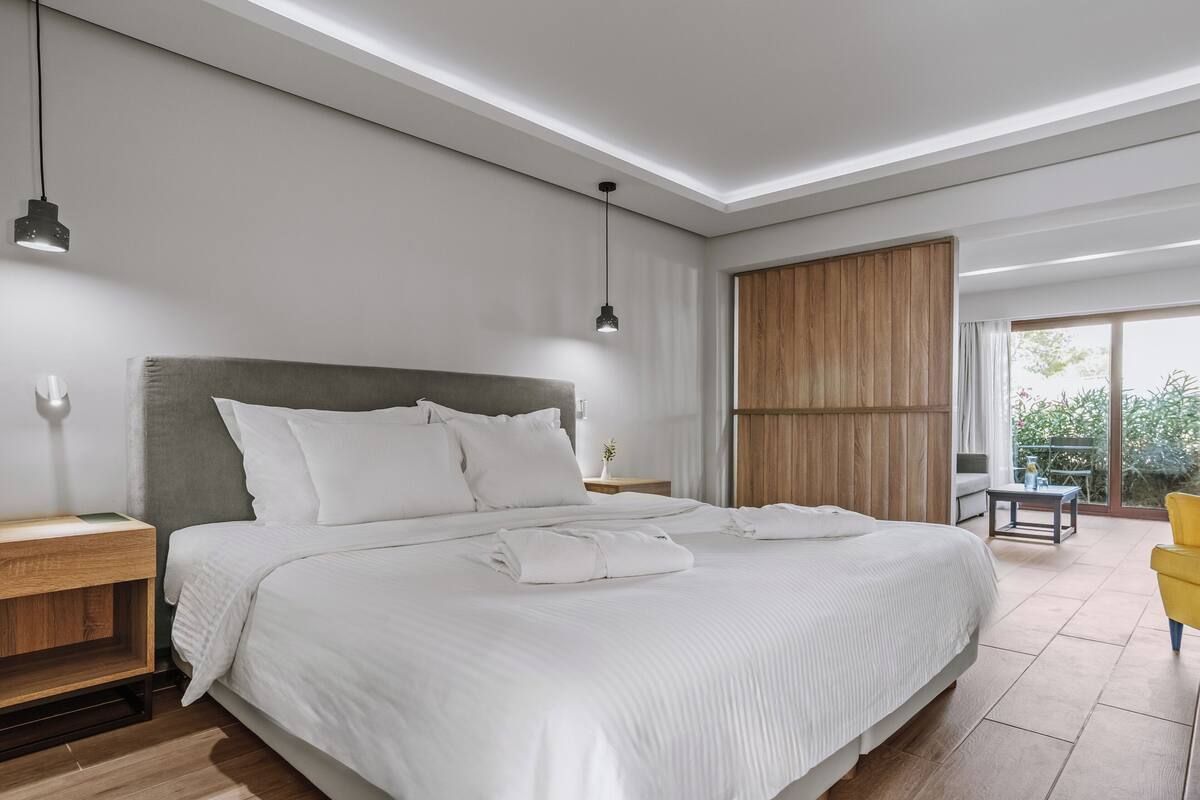 Ein modernes Schlafzimmer mit einem großen Bett, Nachttischen, einem Holzschrank und einem Balkon mit einem gelben Stuhl.
