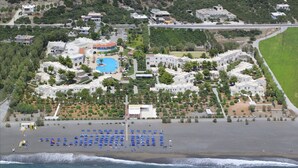 An aerial view of a coastal resort with a swimming pool, beach umbrellas, and multiple buildings. - Almyra Resort (Ierapetra)