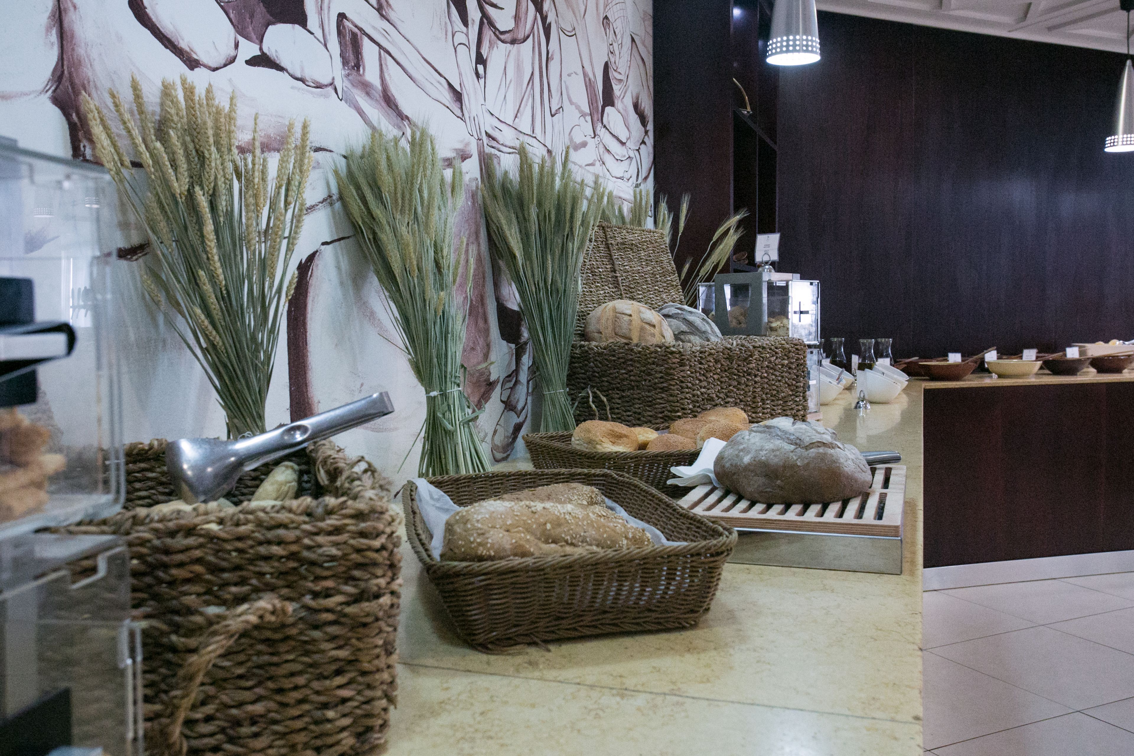 A bakery display with bread and pastries in wicker baskets, a bread slicer, and decorative grasses.