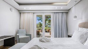 A modern hotel room with a large bed, a seating area, and a view of the outdoors. - Almyra Resort (Ierapetra)