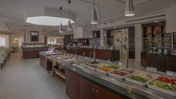 Uma área de buffet com vários pontos de comida, um espelho grande e iluminação pendente.