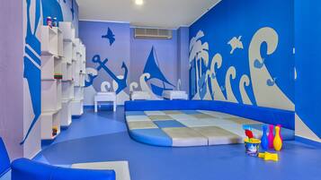 Zona de juegos infantiles con una decoración azul y blanca, que incluye suelo acolchado, zonas de estar y una pared con motivos náuticos.