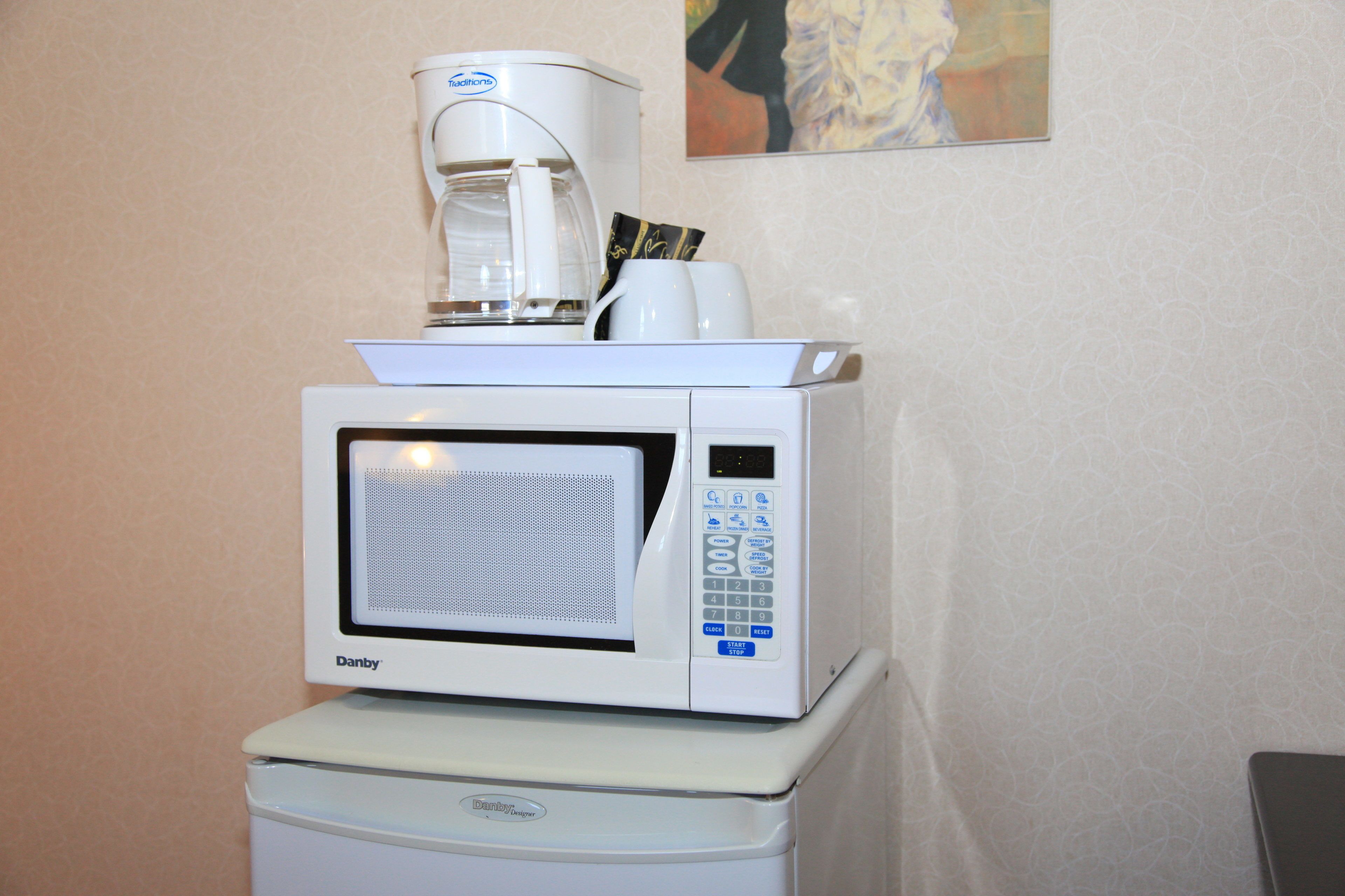 Un horno microondas con una cafetera encima, sobre un pequeño electrodoméstico blanco.
