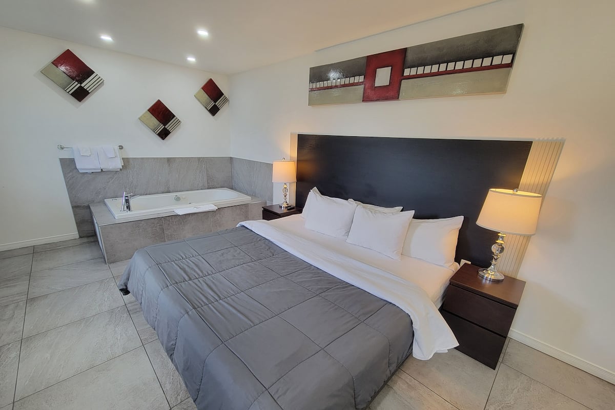 A modern bedroom with a large bed, a separate bathroom with a bathtub, and artwork on the walls.
