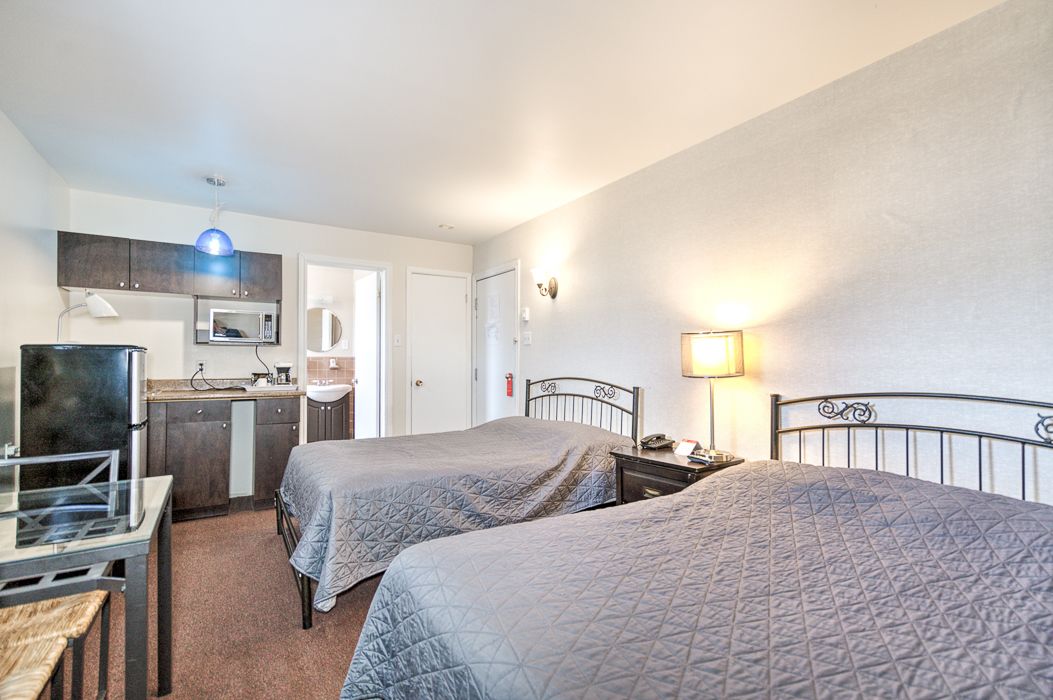 Een hotelkamer met twee bedden, een kitchenette, een bureau en een eettafeltje.