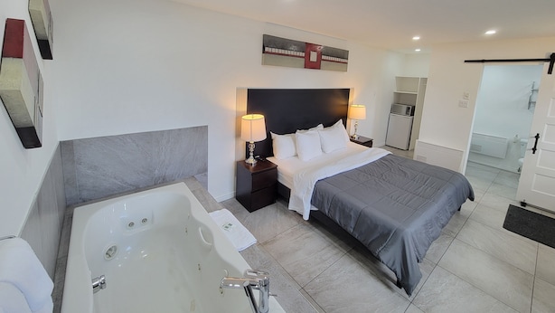 A modern hotel room with a large bed, a separate bathroom with a bathtub, a small desk, and a refrigerator. - Motel Grande ile (Salaberry De Valleyfield)