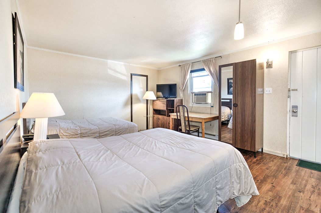 A hotel room with two beds, a desk, a chair, a TV, and a wardrobe.