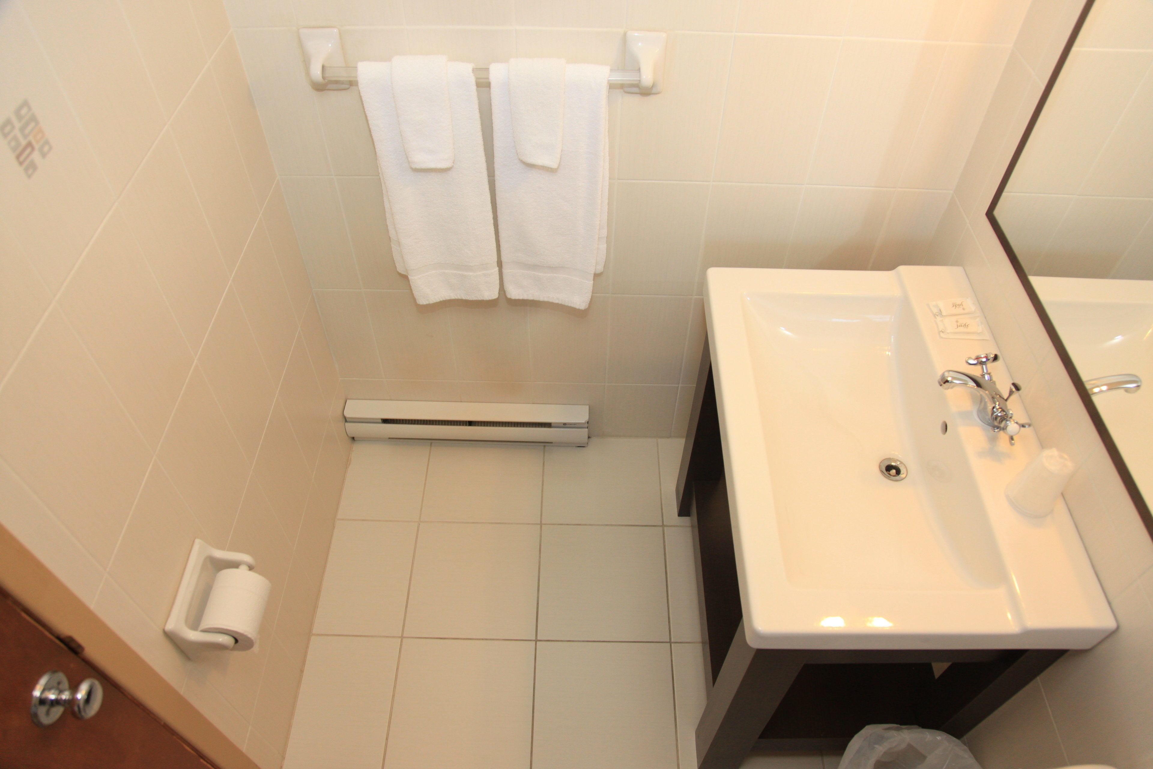 Un baño con un lavamanos blanco, un espejo y dos toallas blancas colgadas en un perchero.